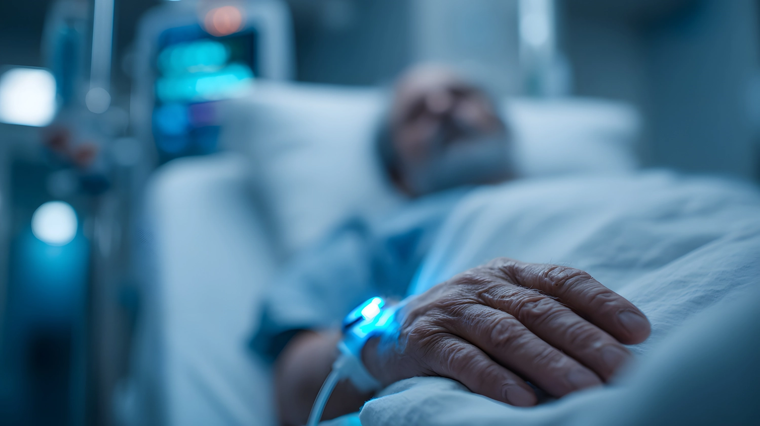 Curanus GmbH – Pflege – Älterer Patient ruht im Krankenhausbett mit Infusion und medizinischem Monitor im Hintergrund.